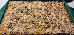 Green cookie sheet containing a large golden-brown baked eight-layer cookie bar prior to being cut.