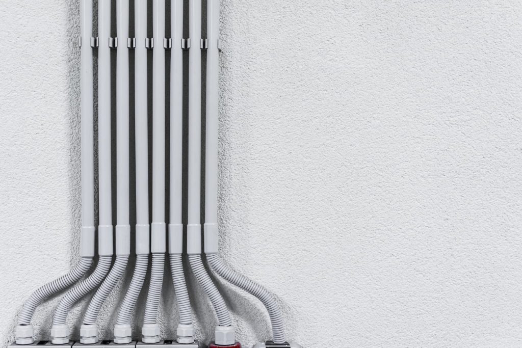 Neatly sorted grouping of gray pipes running down a white wall.